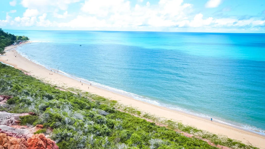Faixa de areia e mar azul de Arraial d'Ajuda vistos do alto da falésia, em Porto Seguro (BA)