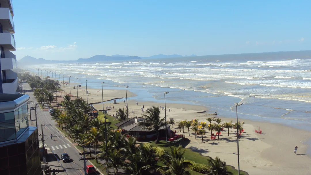 Orla arborizada e faixa de areia da Praia do Caiçara vistas do alto, em Praia Grande (SP)