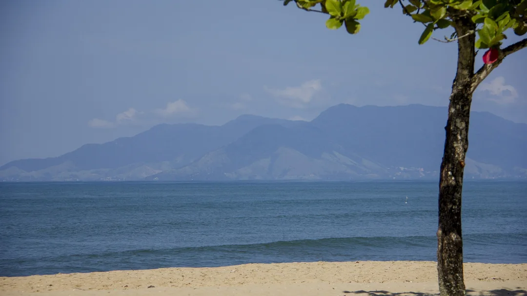 Areia e mar calmo da Praia da Cocanha, com Ilhabela ao fundo, em Caraguatatuba (SP)