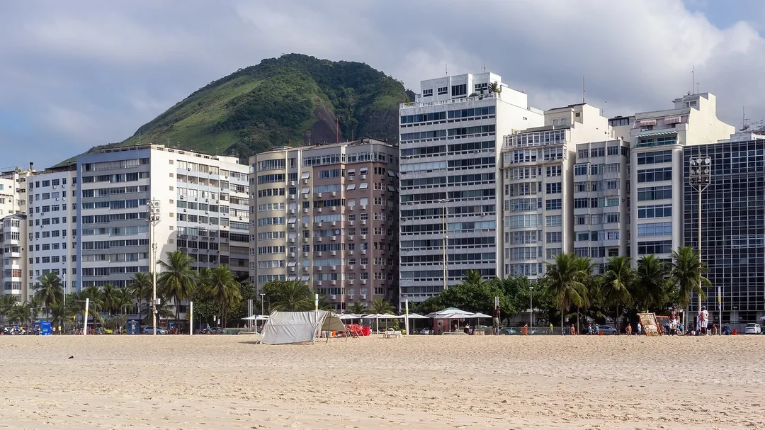Areia e prédios da orla de Copacabana com morro ao fundo, no Rio de Janeiro