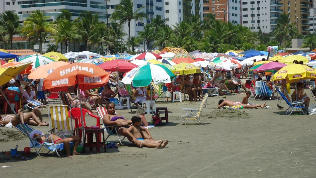 Guarda-sóis coloridos e banhistas na areia da Praia da Guilhermina, diante dos prédios da orla, em Praia Grande (SP)