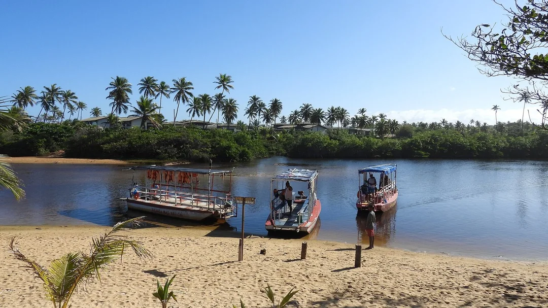 Rio Imbassaí com barcos e coqueiral, a poucos passos do mar, em Mata de São João (BA)