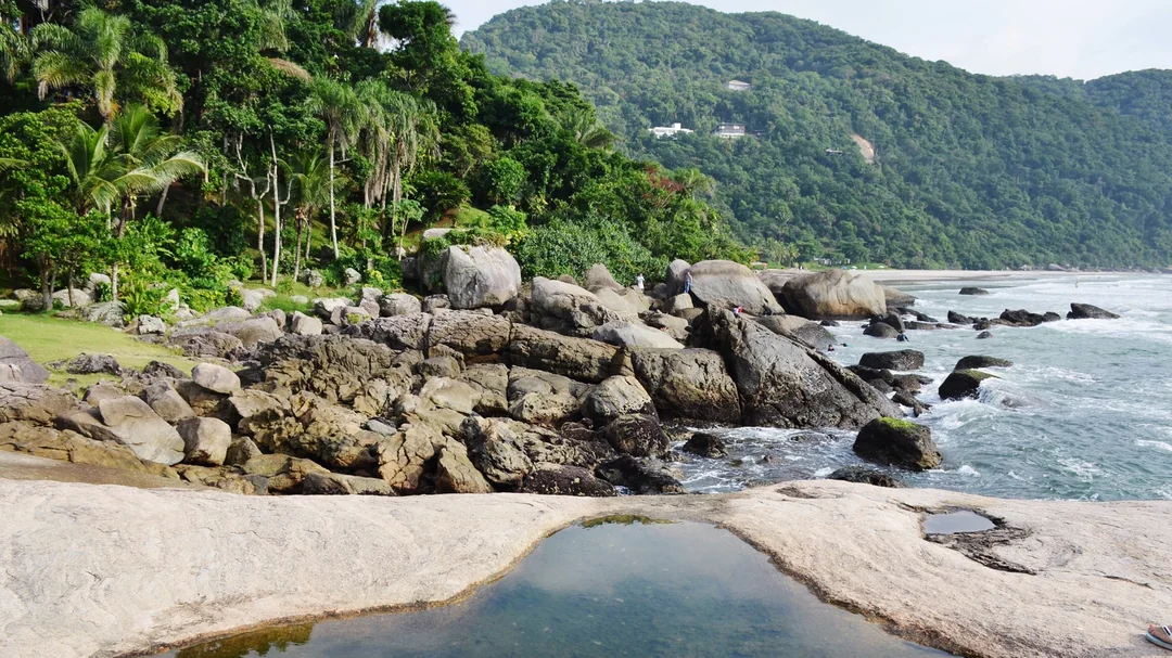 Pedras e poça de água ao lado da areia na Praia de Iporanga, em Guarujá (SP)