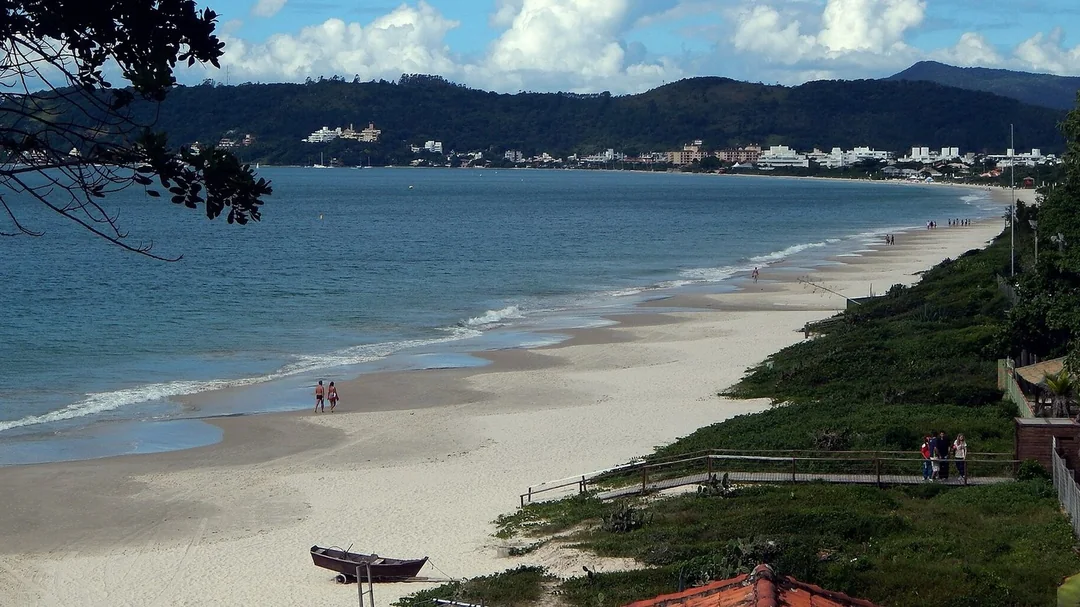 Praia de Jurerê vista do alto, com mar calmo e morros ao fundo, em Florianópolis (SC)