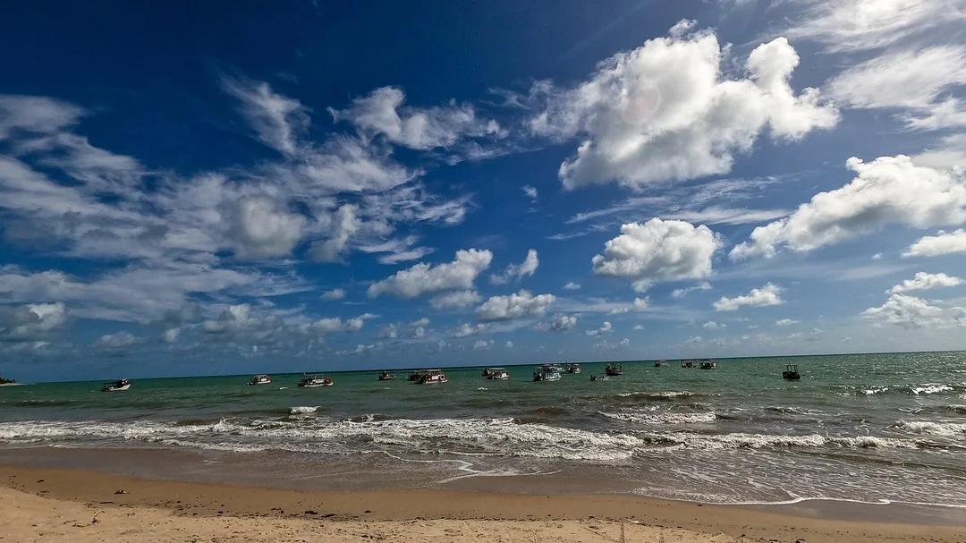 Areia e mar sob céu azul com nuvens na praia de Maracajaú (RN)