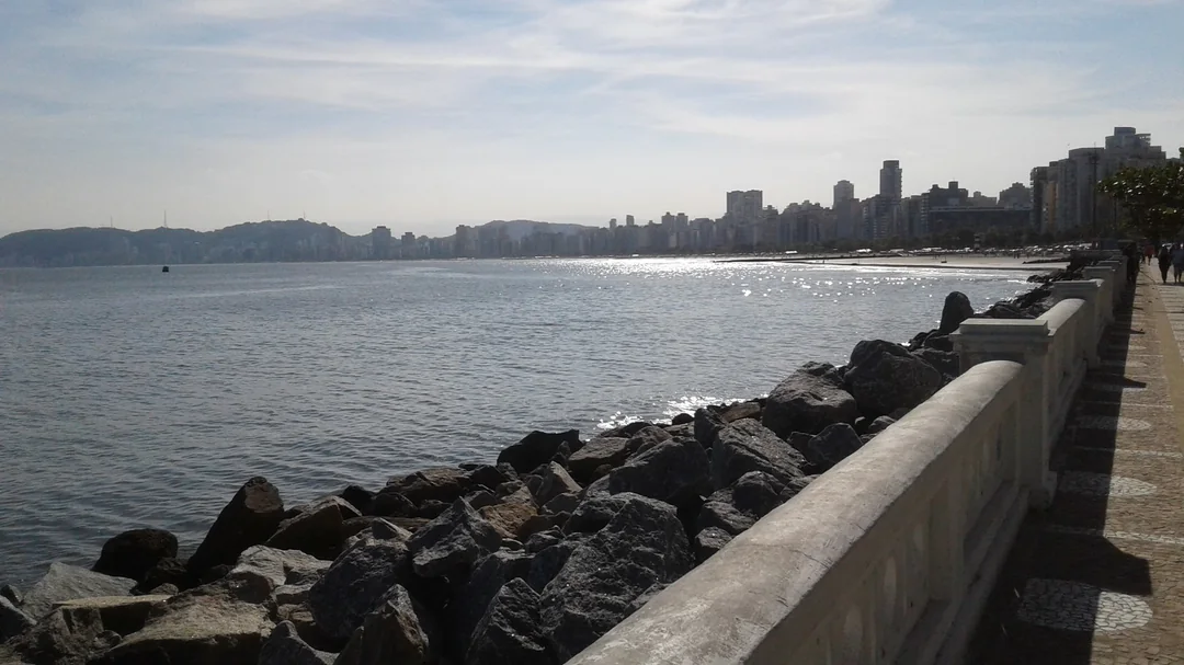 Mureta e pedras da orla da Ponta da Praia, com os prédios da cidade ao fundo, em Santos (SP)