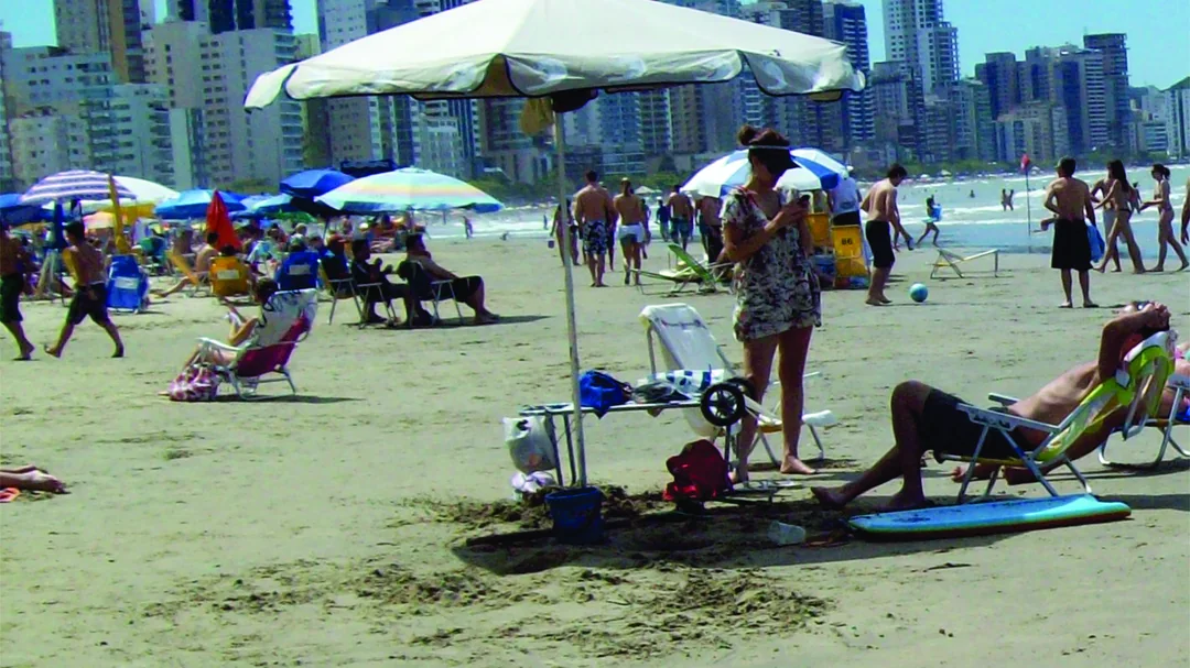 Banhistas e guarda-sóis na areia da Praia Central, com os prédios da orla ao fundo, em Balneário Camboriú (SC)