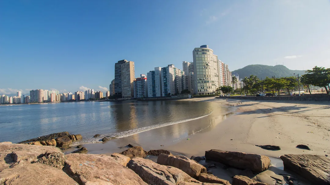 Praia dos Milionários de São Vicente, em São Vicente (SP): Pedras e areia da Praia dos Milionários, com prédios ao fundo, em São Vicente (SP)