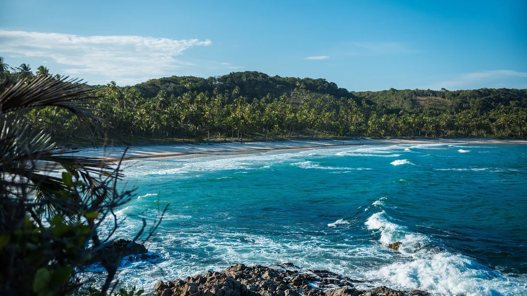 Ondas e mar azul da Prainha, cercada de mata atlântica, em Itacaré (BA)