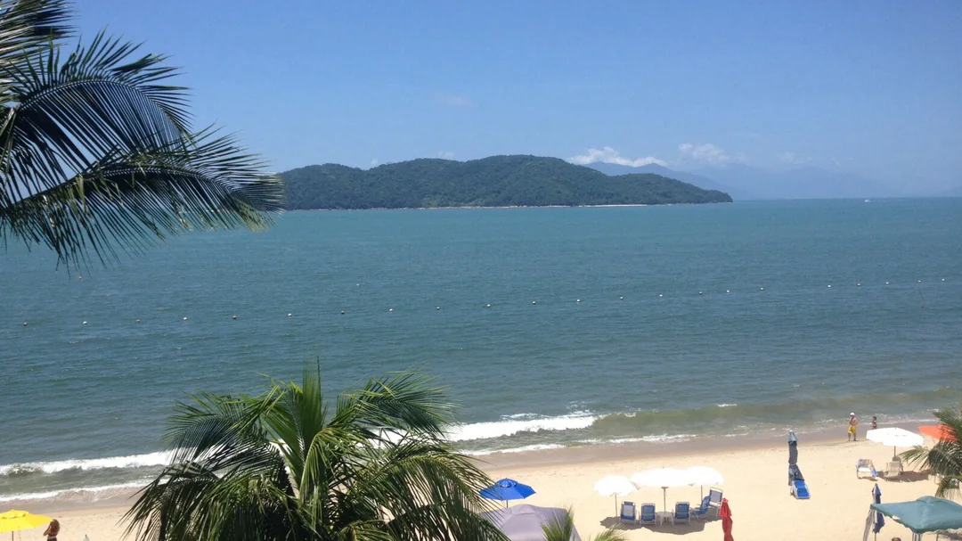 Banhistas e guarda-sóis na areia da Praia da Tabatinga, com uma ilha ao fundo, em Caraguatatuba (SP)